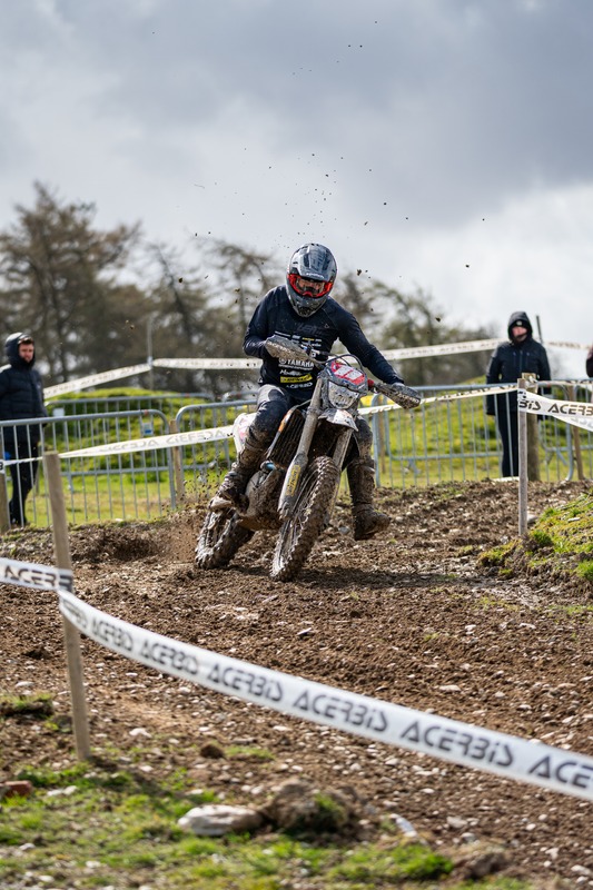 Enduro rider rounding a muddy taped course